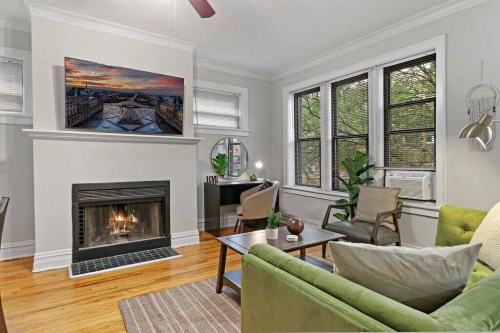 Cozy living room with a fireplace, green sofa, and large windows, featuring a modern art piece above the mantel.