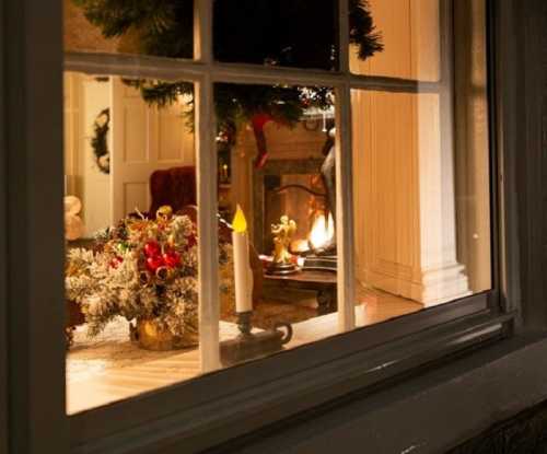 A cozy holiday scene viewed through a window, featuring a festive table arrangement and a warm fireplace glow.