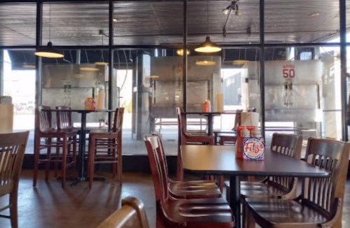 Interior of a casual dining restaurant with wooden tables and chairs, featuring a large glass window and condiment stations.