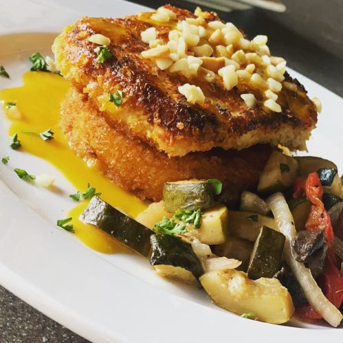 A plate featuring golden-brown fritters topped with chopped nuts, accompanied by colorful sautéed vegetables and a sauce.
