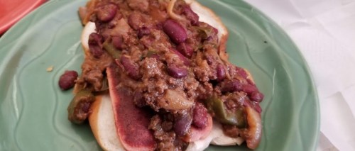 A plate featuring a hot dog topped with chili, beans, and sliced peppers on a bun.