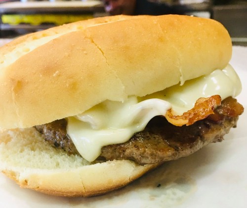 A close-up of a sandwich featuring a beef patty, mayonnaise, and crispy bacon in a soft bun.