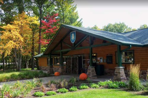 A rustic wooden building surrounded by colorful autumn trees and pumpkins in a landscaped garden.
