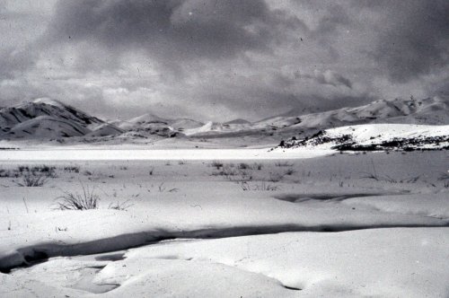 A monochrome landscape of snow-covered hills and a cloudy sky, creating a serene, wintry scene.