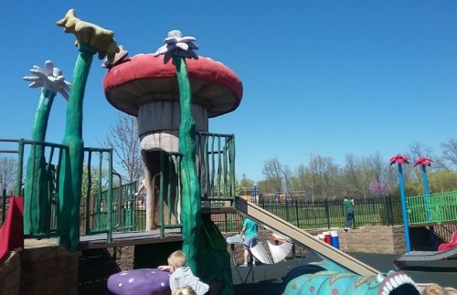Colorful playground structure with a mushroom theme, featuring slides and climbing areas, under a clear blue sky.