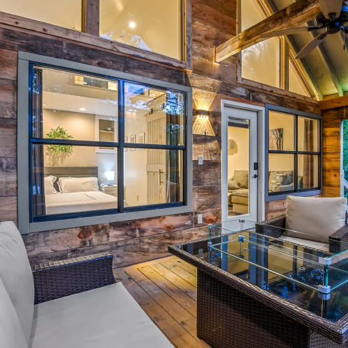 Cozy interior with wooden walls, large windows, and a glass coffee table in a well-lit living space.