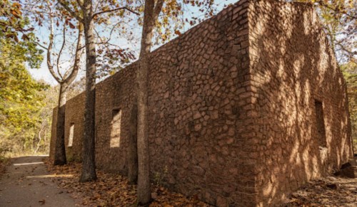 A weathered stone building surrounded by trees and fallen leaves on a sunny day.