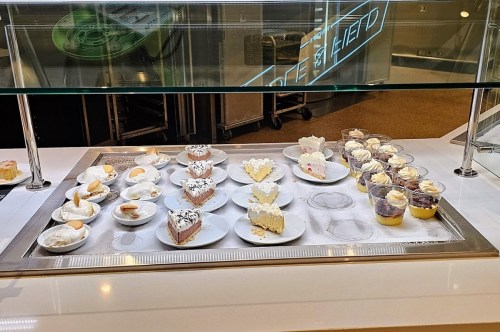 A display of various desserts, including cakes and cups of mousse, arranged on white plates in a glass case.