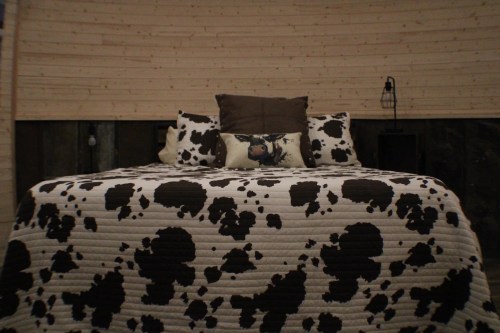 Cozy bedroom featuring a cow-print bedspread and pillows against a wooden wall backdrop.