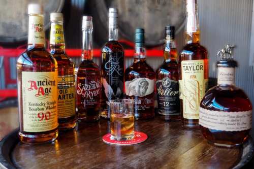 A selection of bourbon bottles arranged on a wooden table, with a glass of whiskey in front.