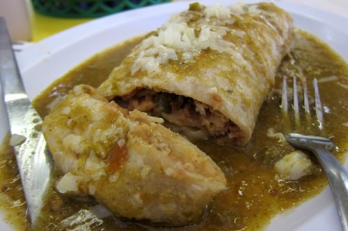 A plate of enchiladas smothered in green sauce, topped with chopped onions, with a fork and knife beside it.