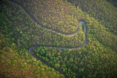 Aerial view of a winding road through lush green forested hills.