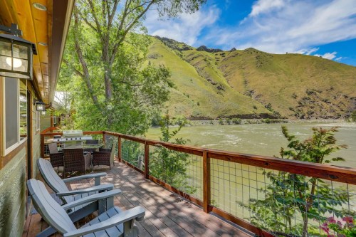 A scenic view from a deck overlooking a river, surrounded by lush green hills and blue skies.