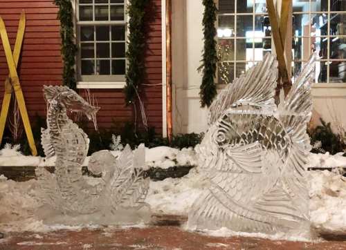 Two intricate ice sculptures of a dragon and a fish, set against a snowy backdrop with festive decorations.