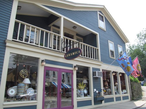 A blue building with a sign reading "Ceramica," featuring large windows displaying ceramic items and flags outside.