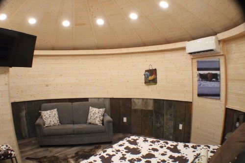 Cozy interior of a circular room featuring a sofa, artwork, and wooden walls with modern lighting.