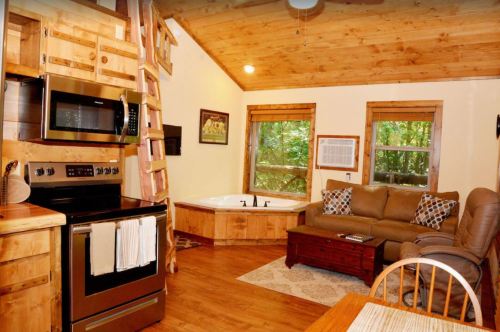 Cozy cabin interior with wooden decor, a kitchen, living area, and a jacuzzi by the windows.