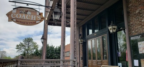 Exterior view of Coach's restaurant, featuring a wooden sign and decorative lanterns, with a brick facade and large windows.