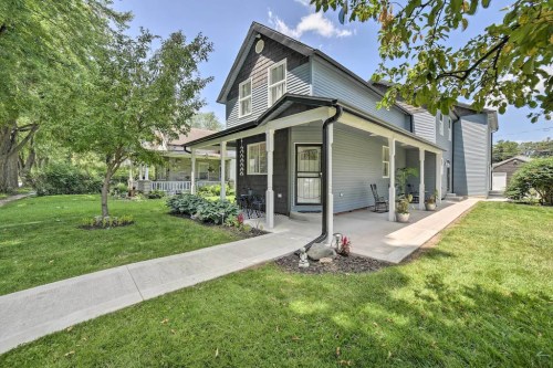 A charming two-story house with a green lawn, pathway, and porch surrounded by trees and shrubs on a sunny day.