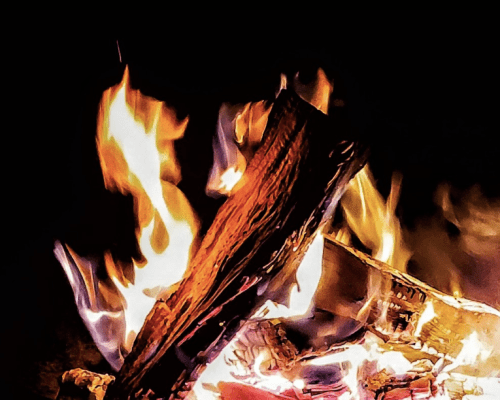 A close-up of a crackling fire with vibrant flames and glowing embers against a dark background.