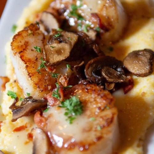 Seared scallops on creamy grits, topped with sautéed mushrooms and garnished with fresh parsley.