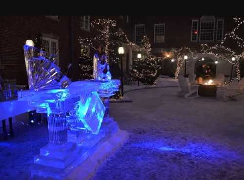 A winter scene featuring an illuminated ice sculpture, surrounded by festive lights and a cozy fire pit.