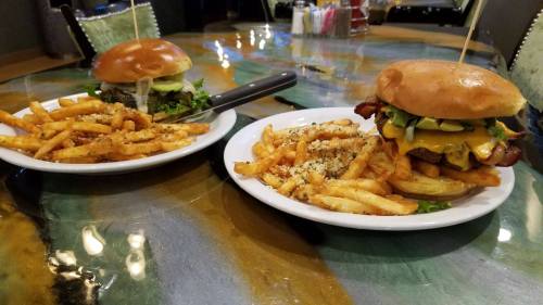 Two plates on a colorful table: one with a burger and fries, the other with a smaller burger and a side salad.