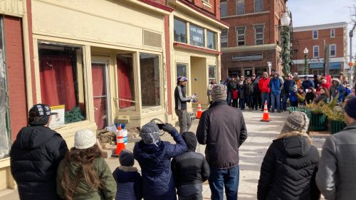 A crowd gathers on a street as a speaker addresses them in front of a historic building.