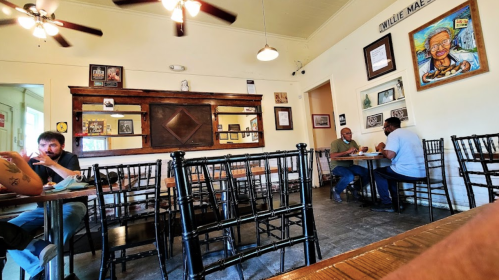 A cozy restaurant interior with wooden tables, black chairs, and framed photos on the walls. Two patrons are seated.