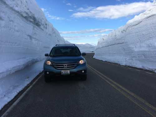 A gray SUV on a snow-covered road, flanked by tall snowbanks under a blue sky.