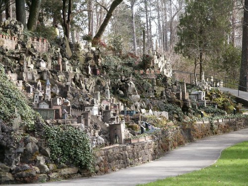 A winding path beside a hillside adorned with miniature buildings and lush greenery in a park setting.
