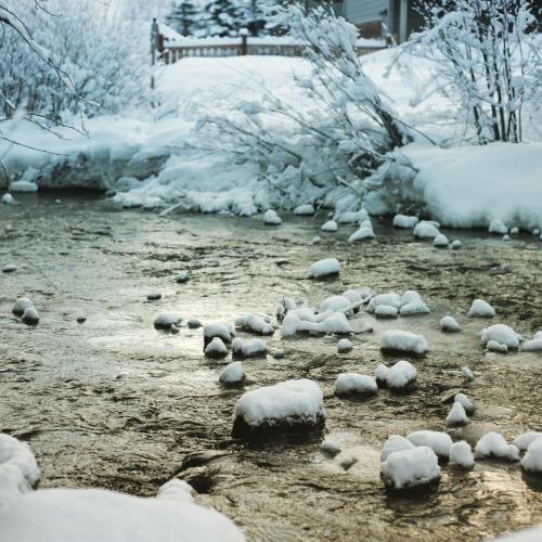 A serene winter scene featuring a gently flowing stream surrounded by snow-covered rocks and frosty trees.
