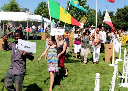 A diverse group of people march in a park, holding signs for Malawi and Senegal, with flags in the background.