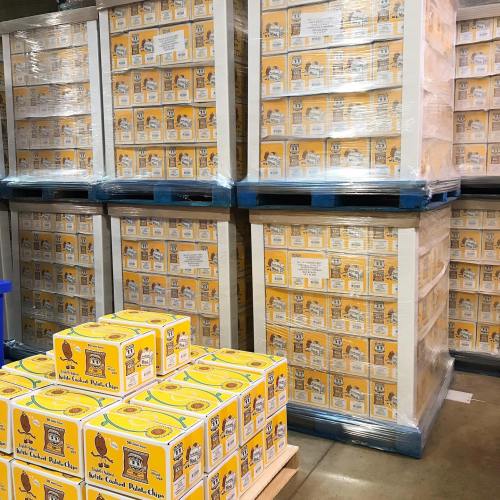 Stacks of yellow boxes of potato chips on pallets in a warehouse setting.
