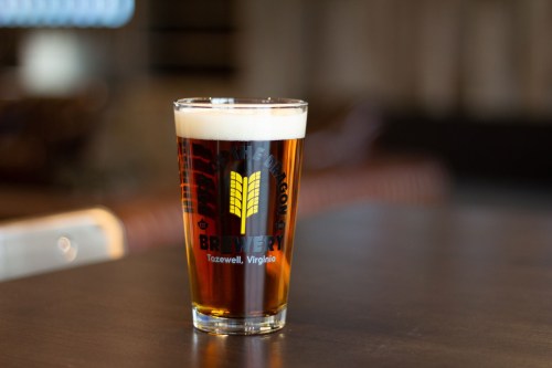 A glass of amber beer with a frothy head, featuring a logo that reads "Brewery" from Tazewell, Virginia.