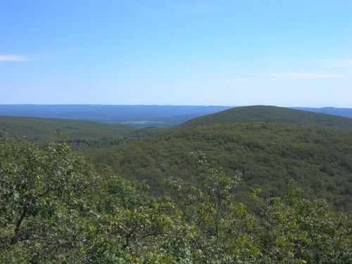 A panoramic view of rolling green hills under a clear blue sky, stretching into the distance.