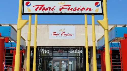 Exterior of Thai Fusion Restaurant, featuring signs for Pho and Boba, with a bright blue sky in the background.