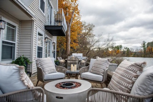 Cozy outdoor seating area by a lake, featuring a fire pit and autumn foliage in the background.