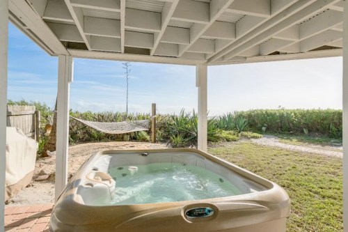 A hot tub under a covered patio, with a view of a hammock and lush greenery in the background.