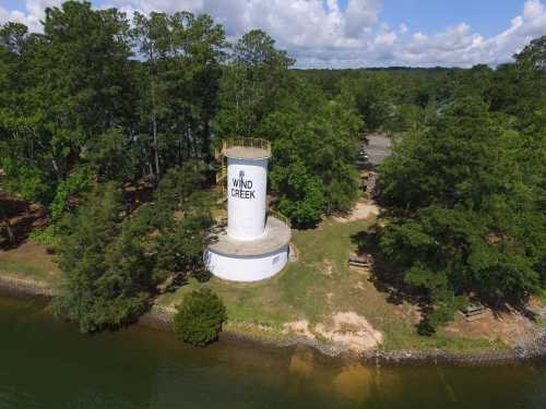 Aerial view of a white water tower labeled "Wind Creek," surrounded by trees and a calm body of water.