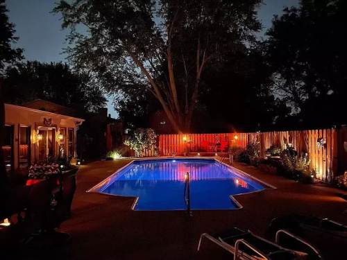 A serene backyard at night featuring a lit pool, surrounded by trees and softly glowing lights.