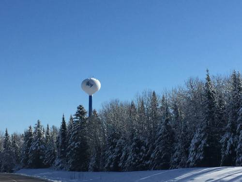 A water tower stands tall among snow-covered trees under a clear blue sky.