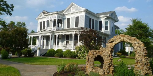 A large, elegant Victorian-style house with a wraparound porch and a stone archway in the foreground.
