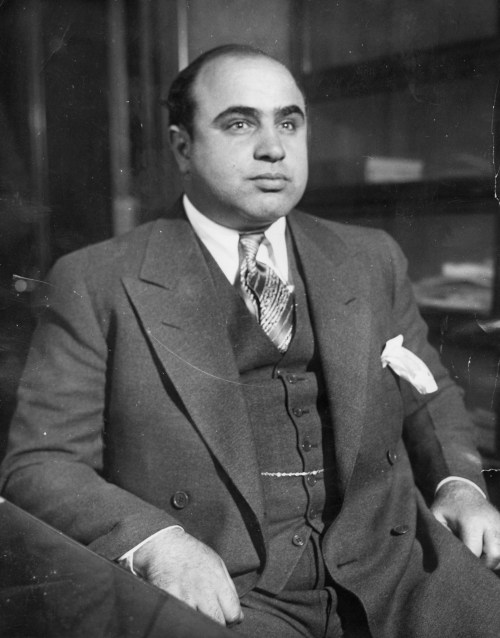 A well-dressed man in a suit sits confidently, looking directly at the camera.
