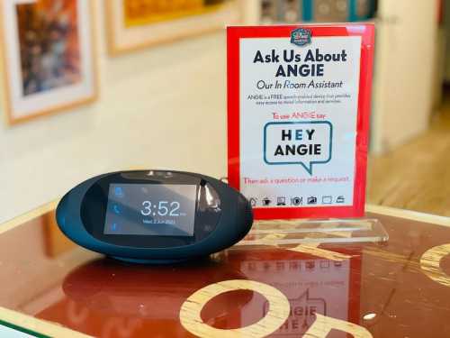 A smart speaker on a table next to a sign promoting "Angie," an in-room assistant service. Time displayed is 3:52.