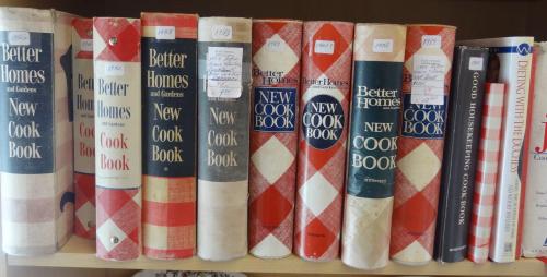 A shelf displaying several vintage cookbooks, mostly titled "Better Homes New Cook Book" in various designs.