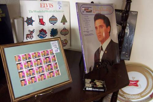 A display featuring Elvis memorabilia, including albums, stamps, and playing cards on a wooden stand.