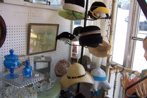A display of various hats in a vintage shop, with a painting and decorative items in the background.
