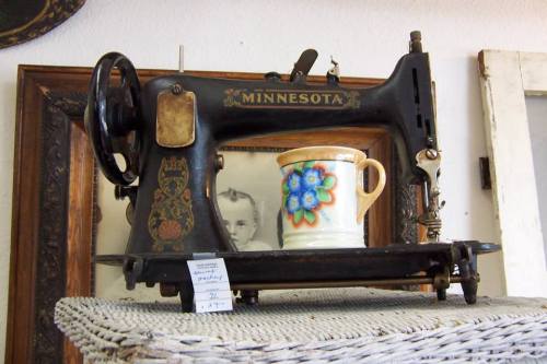 An antique Minnesota sewing machine displayed on a shelf with a colorful ceramic mug beside it.