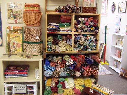 A display of colorful fabric rolls neatly arranged on shelves, alongside baskets and craft books in a cozy craft store.